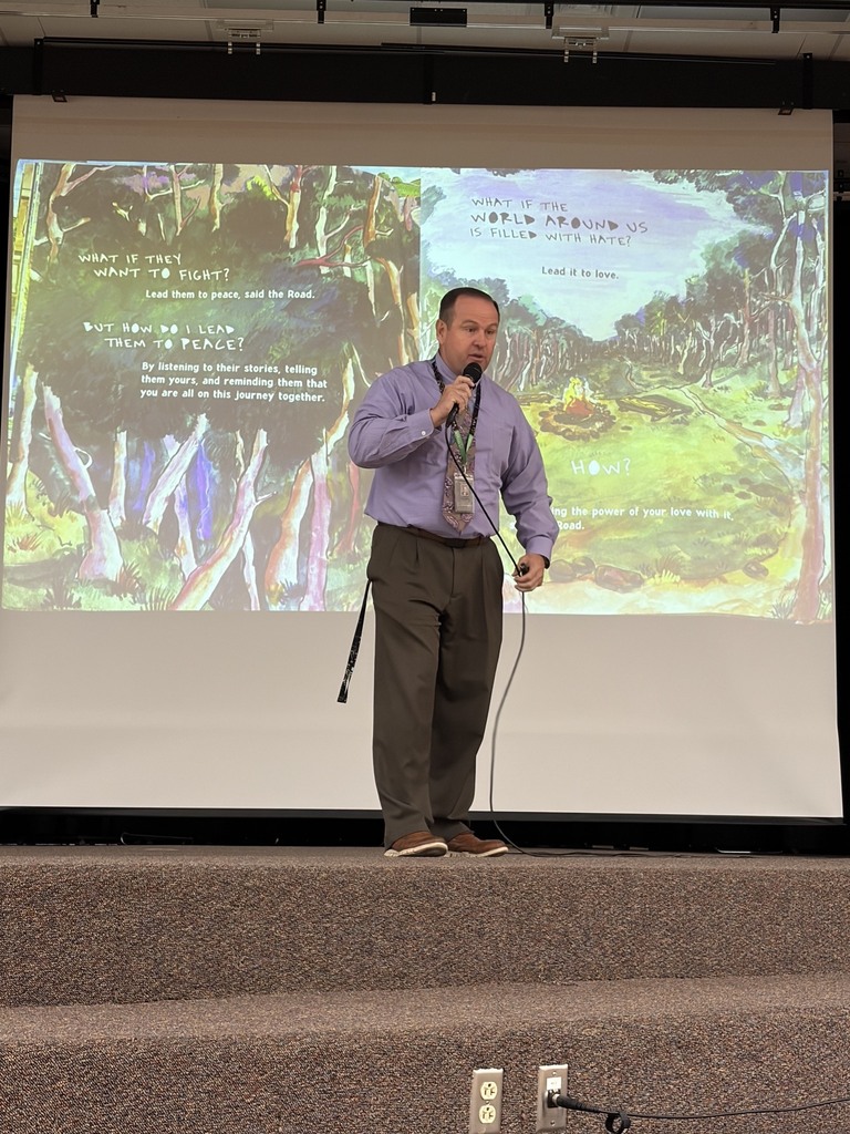 superintendent reading to students, standing in front of book portrayed on the screen