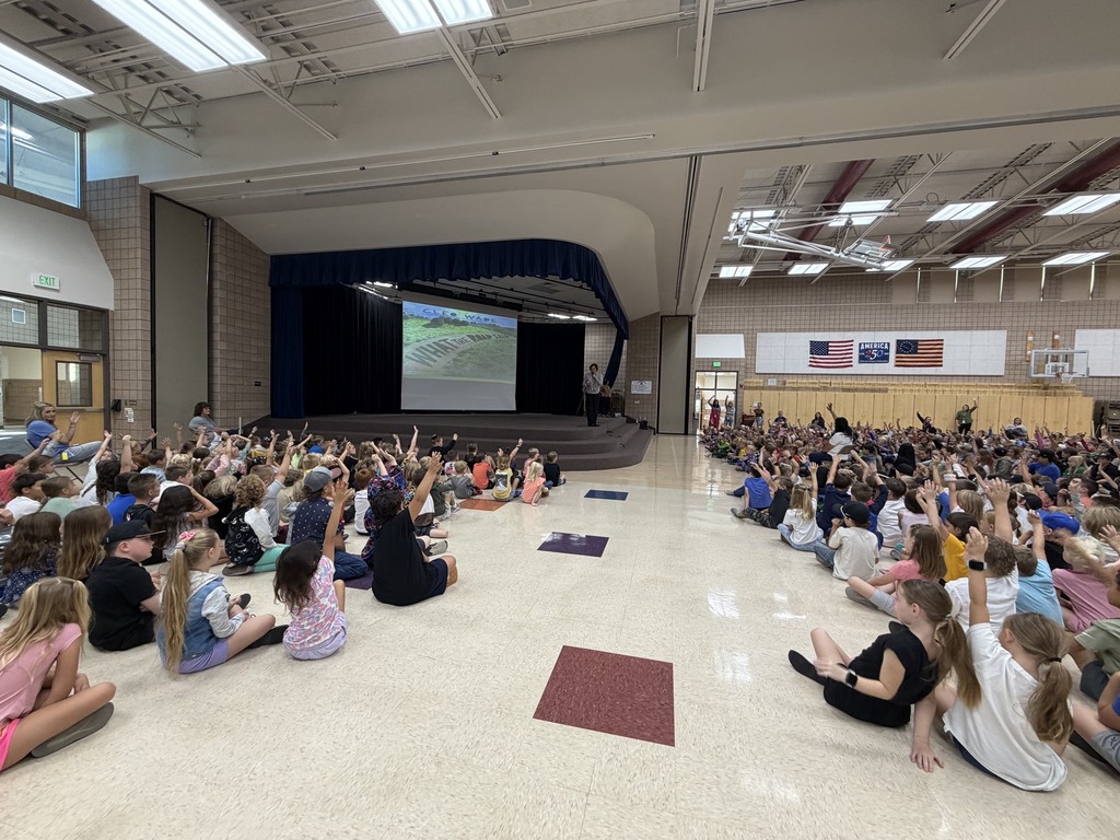 superintendent reading to students, standing in front of book portrayed on the screen