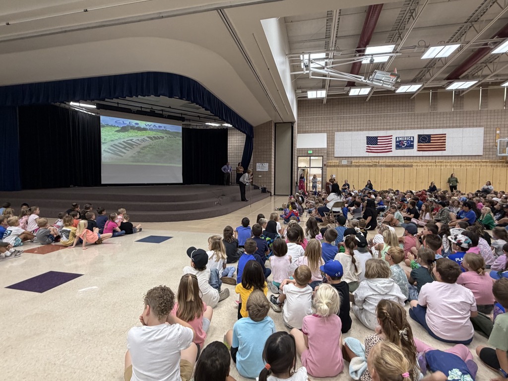 superintendent reading to students, standing in front of book portrayed on the screen