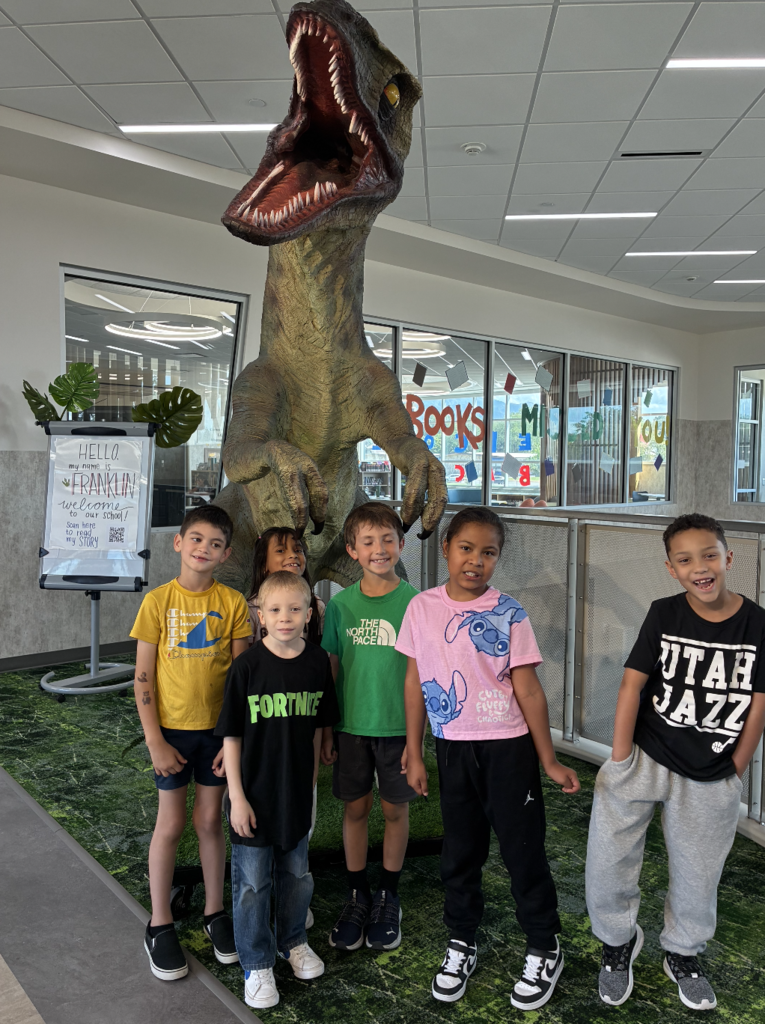 6 students standing in front of a dinosaur statue