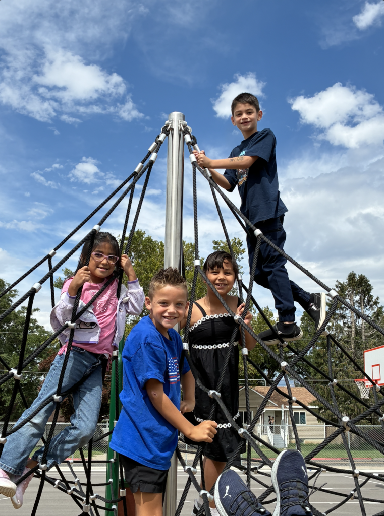 students posing on the climbing web on the playground