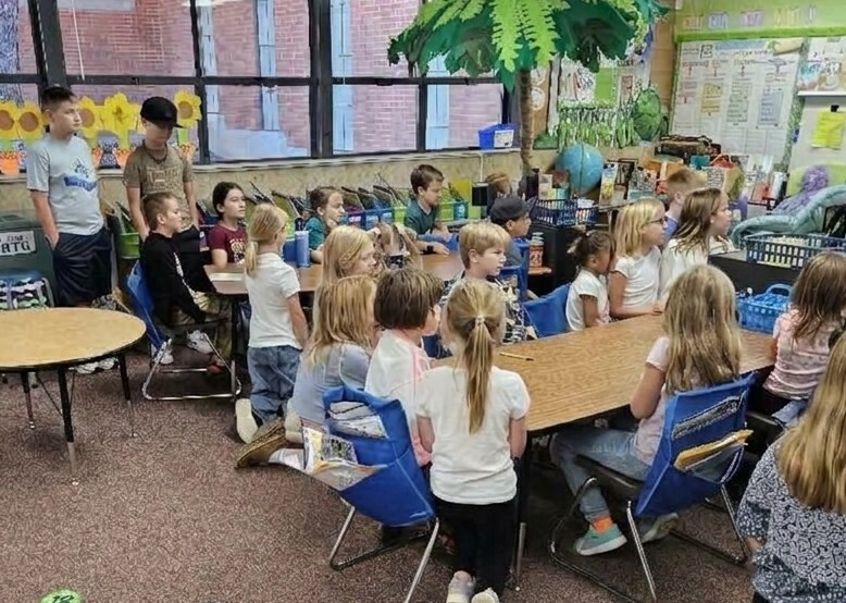 Fifth-grade and first-grade buddy pairs sitting together at classroom desks, engaged in a joint learning activity. 
