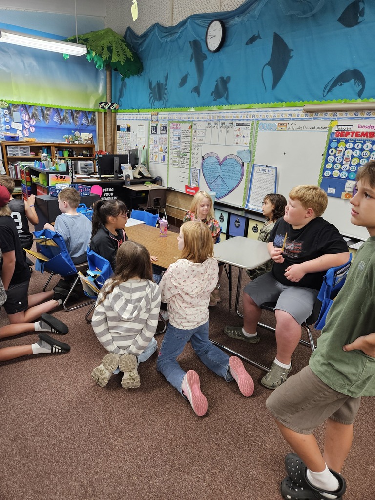 Fifth-grade and first-grade buddy pairs sitting together at classroom desks, engaged in a joint learning activity. 