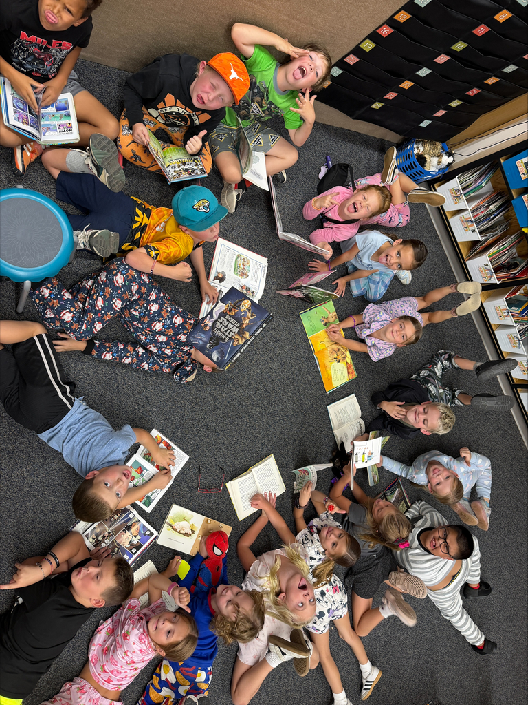 A large group of elementary students gathers on the classroom floor, each reading books in a circle while enjoying a cozy reading activity.