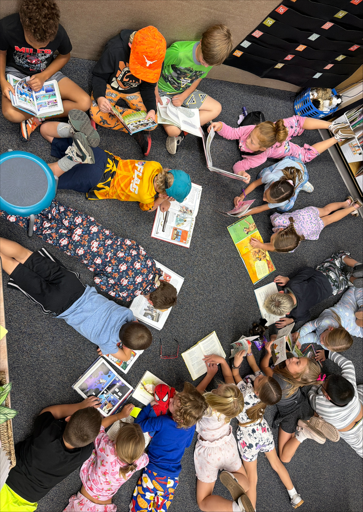 A large group of elementary students gathers on the classroom floor, each reading books in a circle while enjoying a cozy reading activity.