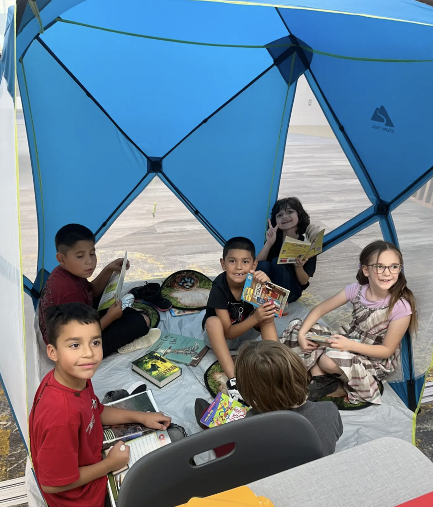5 students sitting in a pop up tent reading