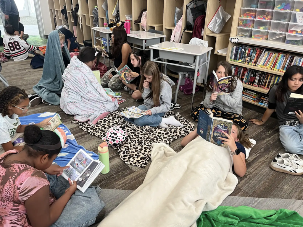 students laying on the floor with blankets and pillows reading books