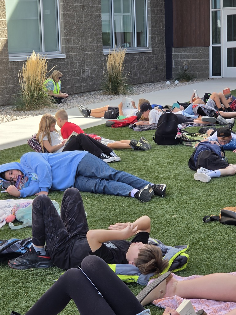 Multiple students lying down and resting or reading on the grass outdoors.   