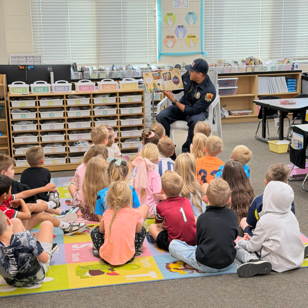 A firefighter sitting in a chair reading to a class of students.