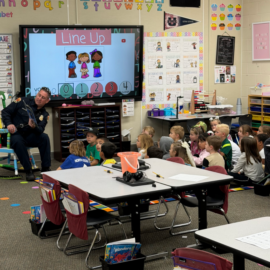 A firefighter sitting in a chair reading to a class of students.