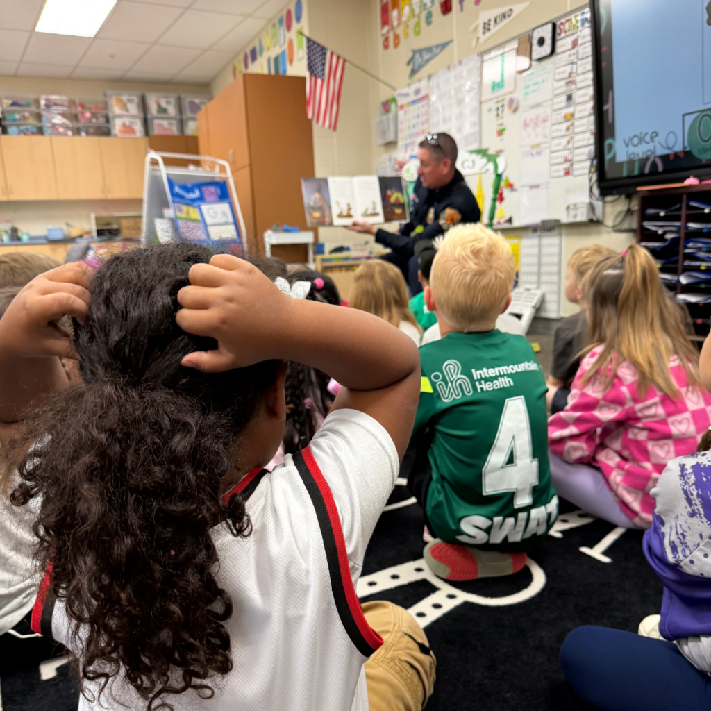 A firefighter sitting in a chair reading to a class of students.