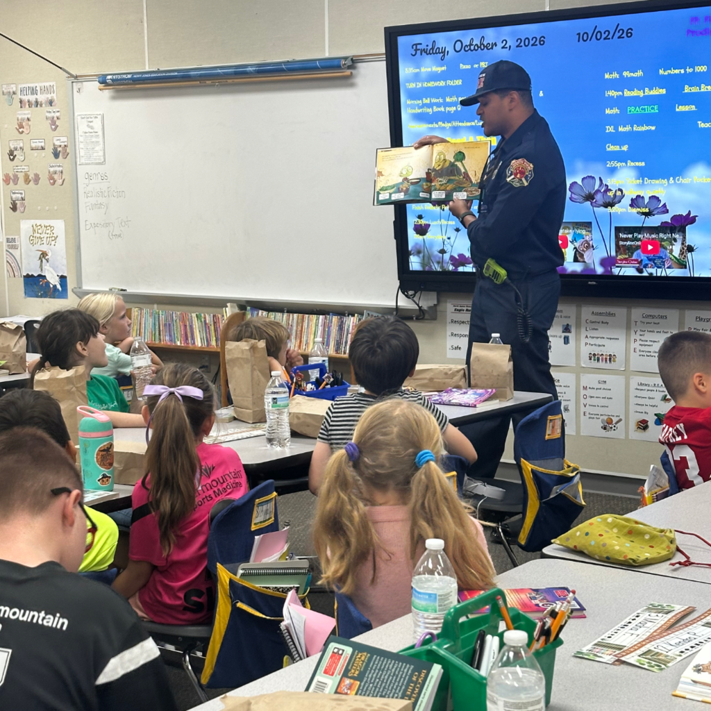A firefighter standing in front of the class reading them a book.