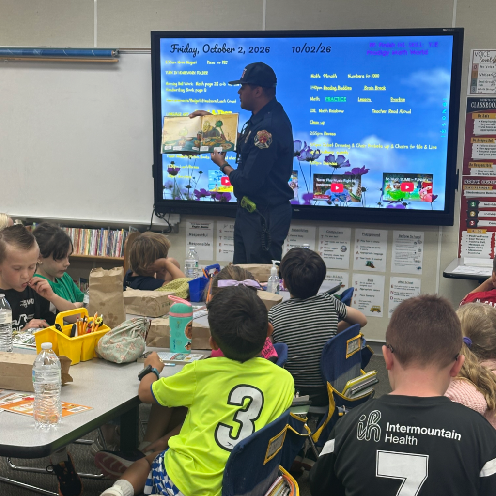 A firefighter standing in front of the class reading them a book.