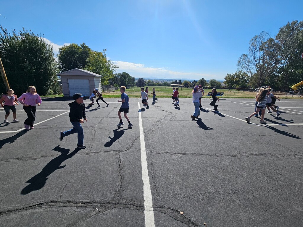 Students demonstrating gas particles by running freely across the open outdoor basketball court.