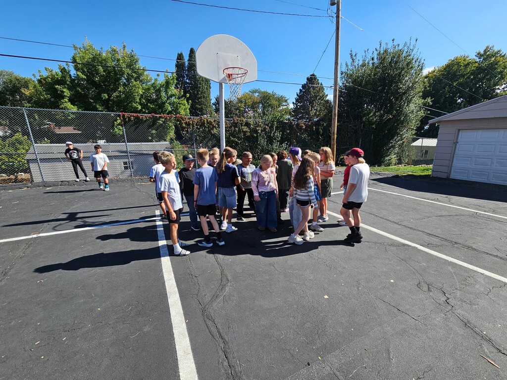 A group of students standing tightly packed together under the basketball hoop to represent solid particles closely bonded in a fixed shape.