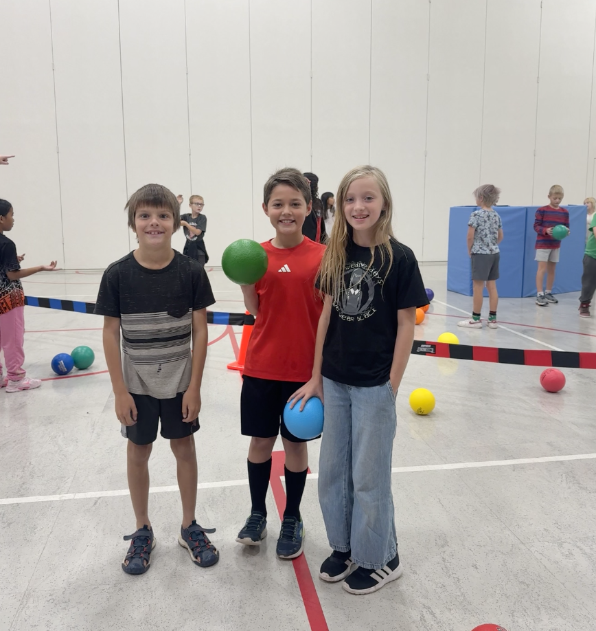 three boys holding P.E. balls standing in the gym smiling