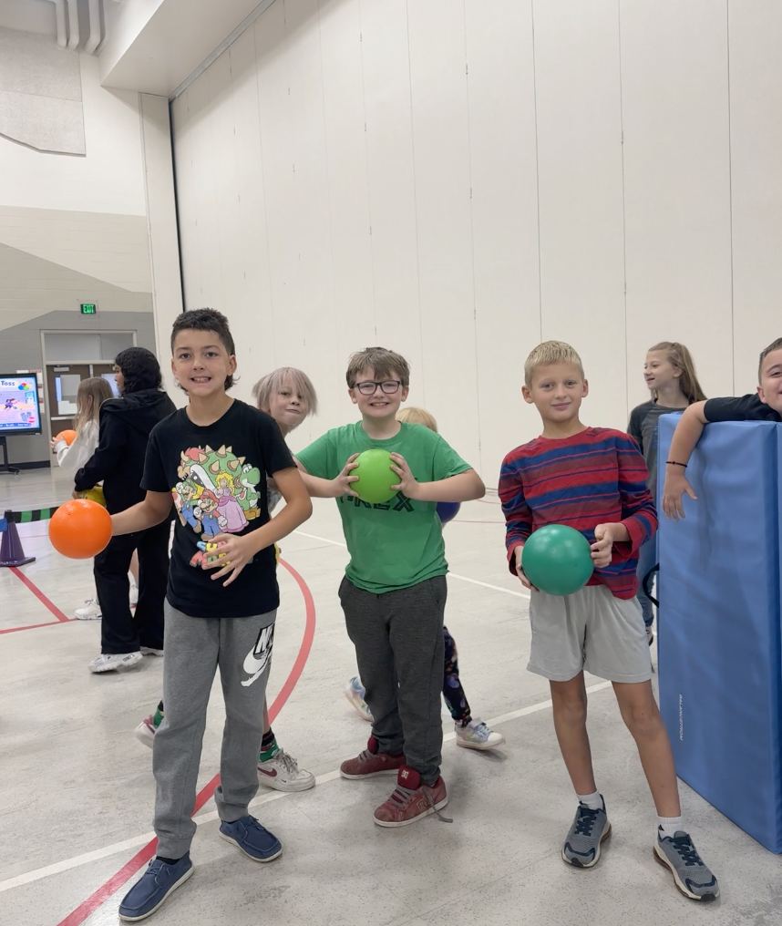 three boys holding P.E. balls standing in the gym smiling