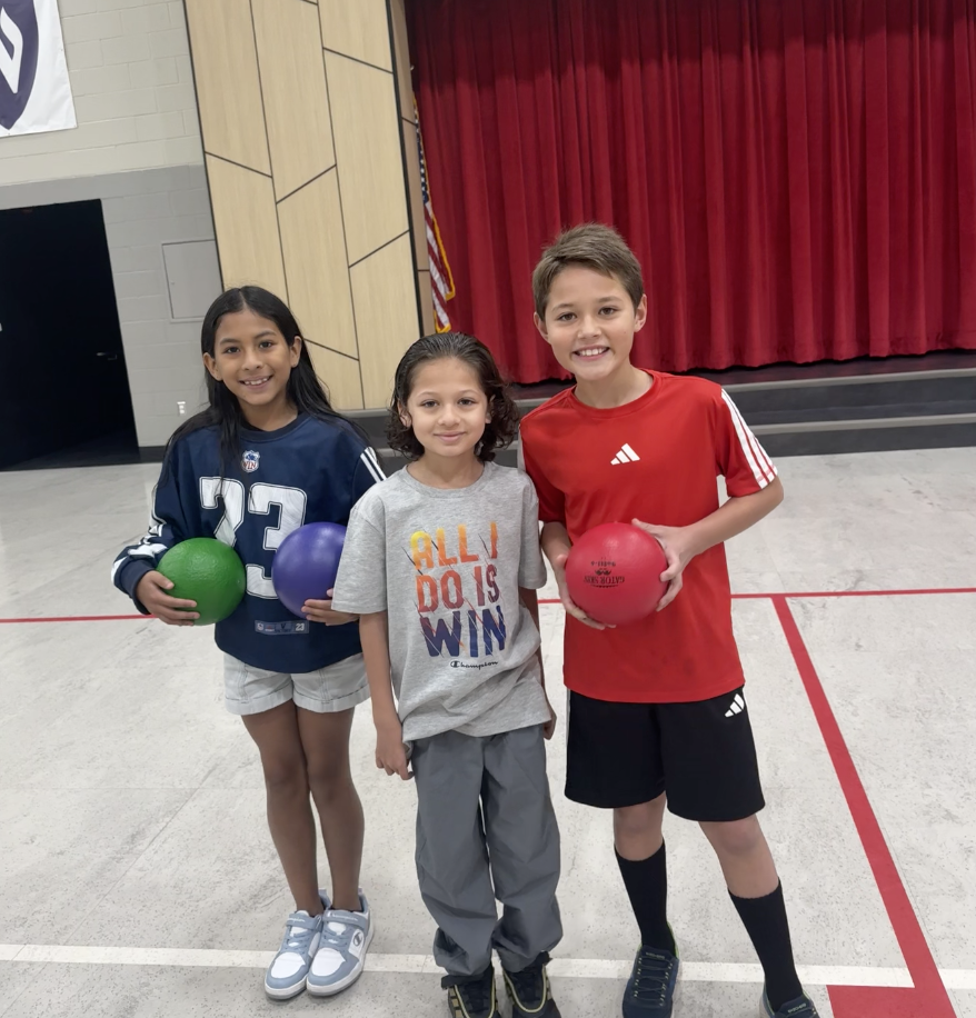 three boys holding P.E. balls standing in the gym smiling
