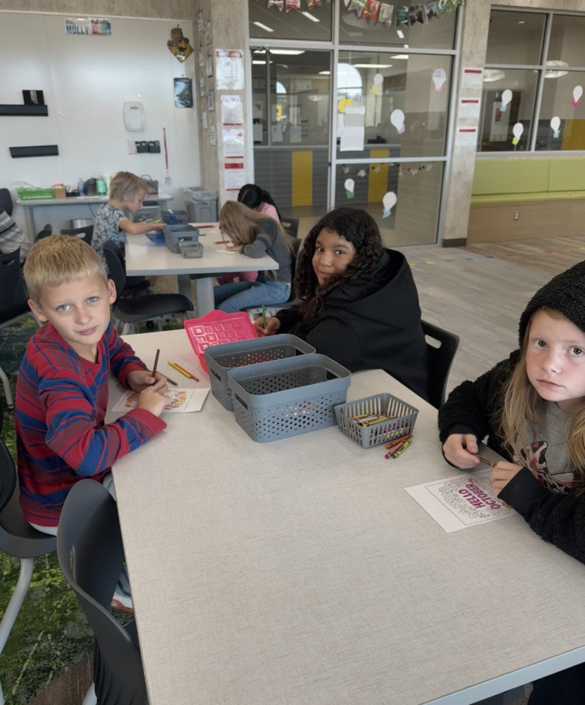 a group of three students sitting at a table in the library coloring