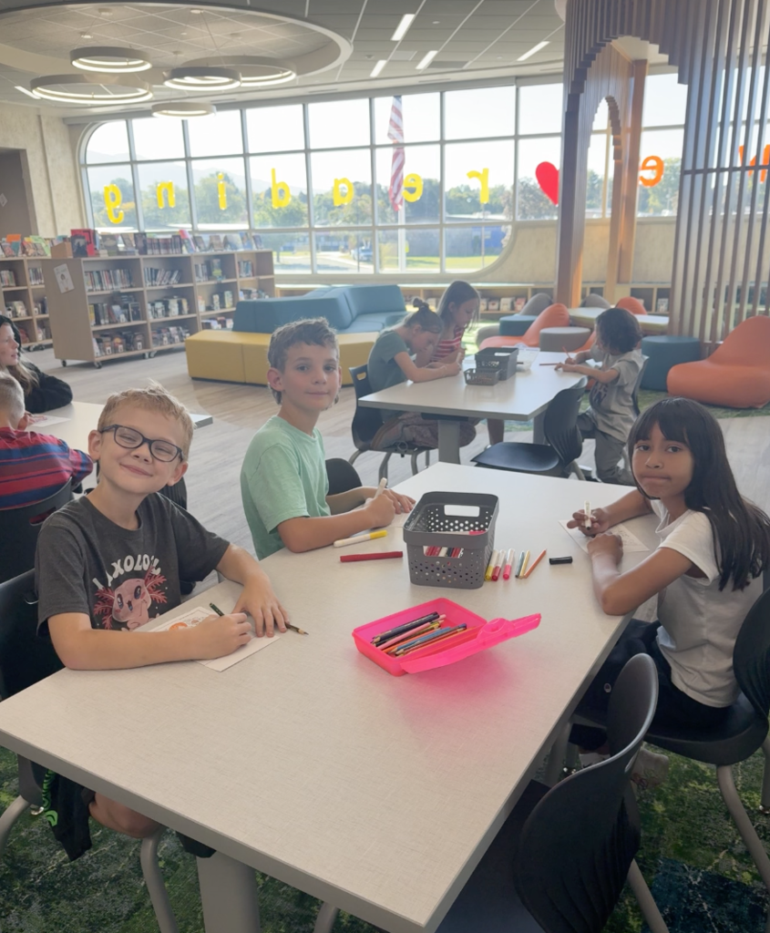a group of three students sitting at a table in the library coloring