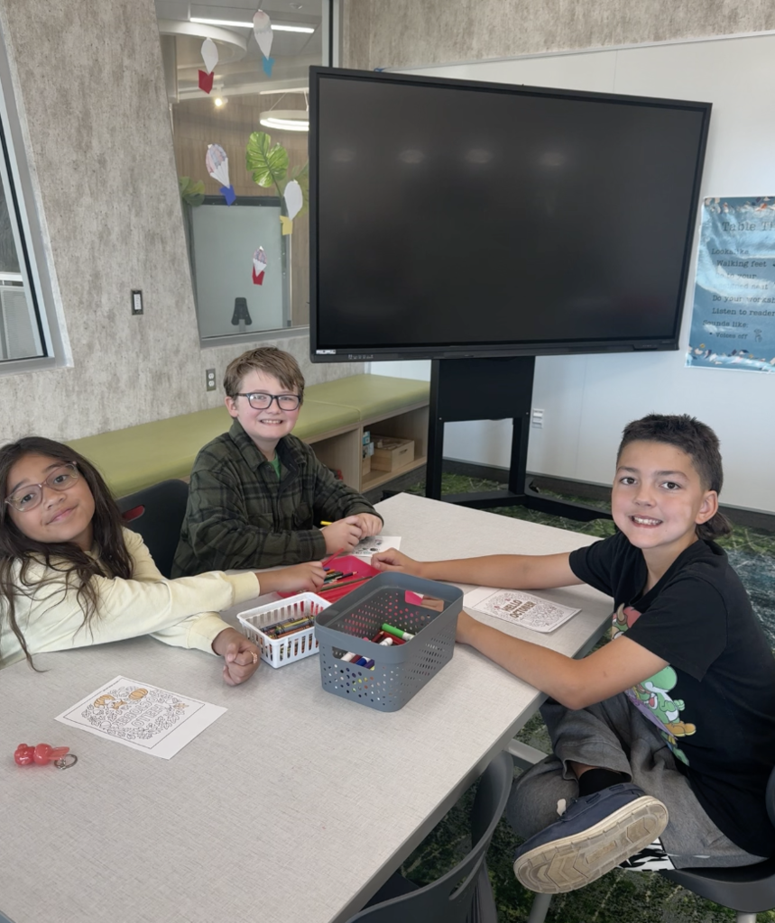 a group of three students sitting at a table in the library coloring