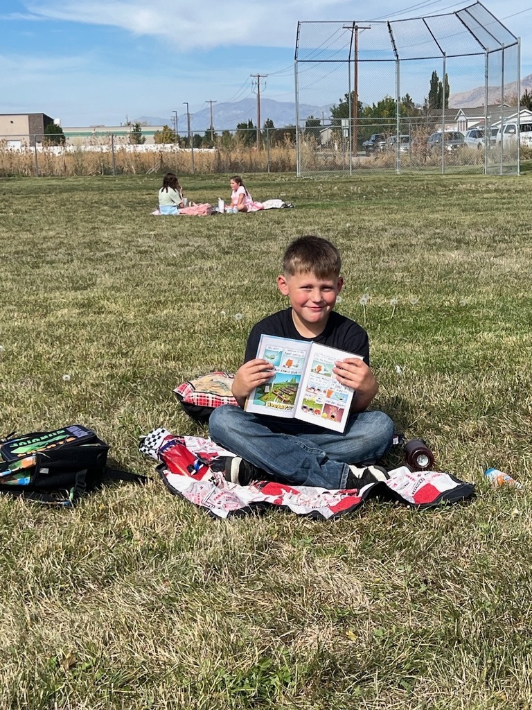 male student smiling holding up a book sitting on the grass