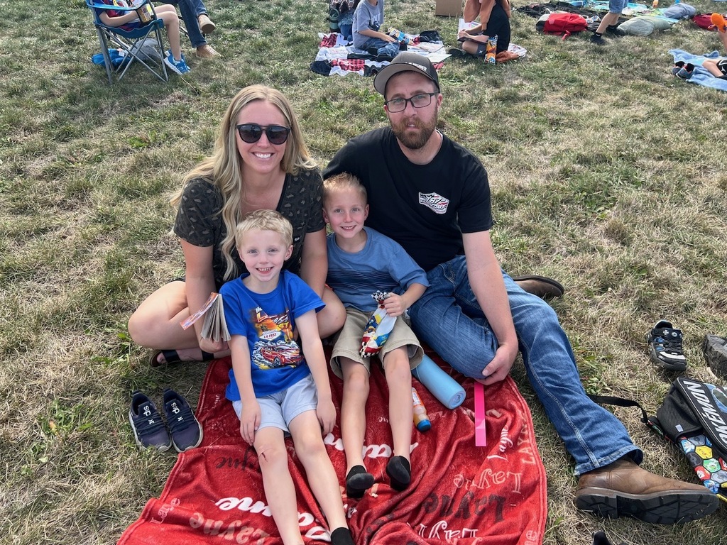 family reading books with their children on a blanket on the grass all are looking at the camera smiling 
