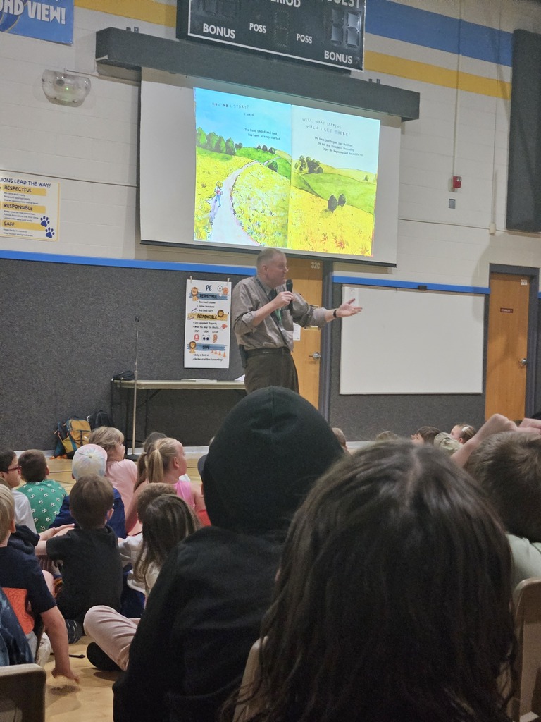 Adminstrator reading a book to a gym full of students. 