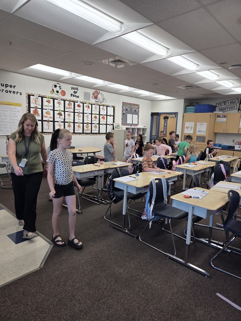 some students are seen sitting and doing work while others are up walking around the room