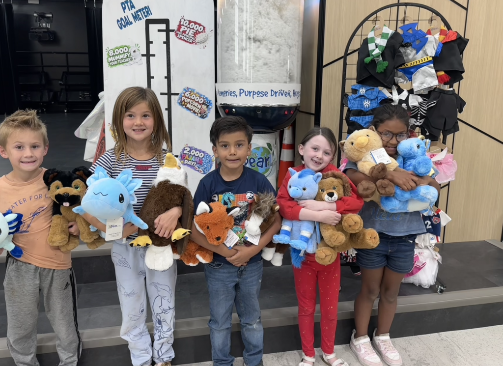 students holding stuffed animals standing in front of a cotton stuffing machine