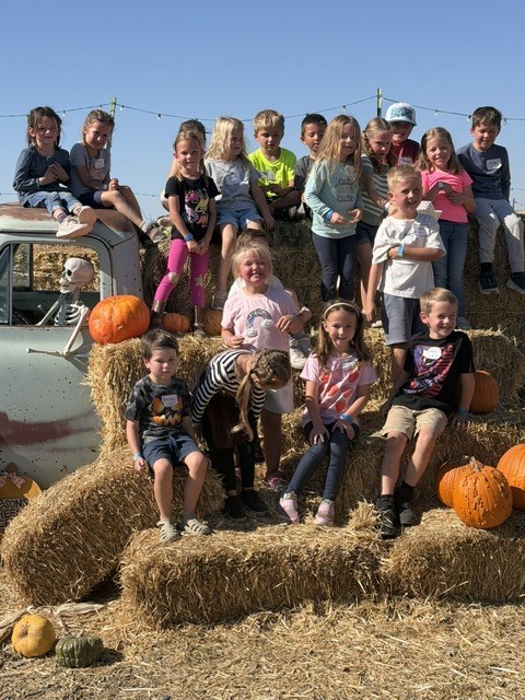 Captures the whole group on hay bales next to the vintage truck and pumpkins.