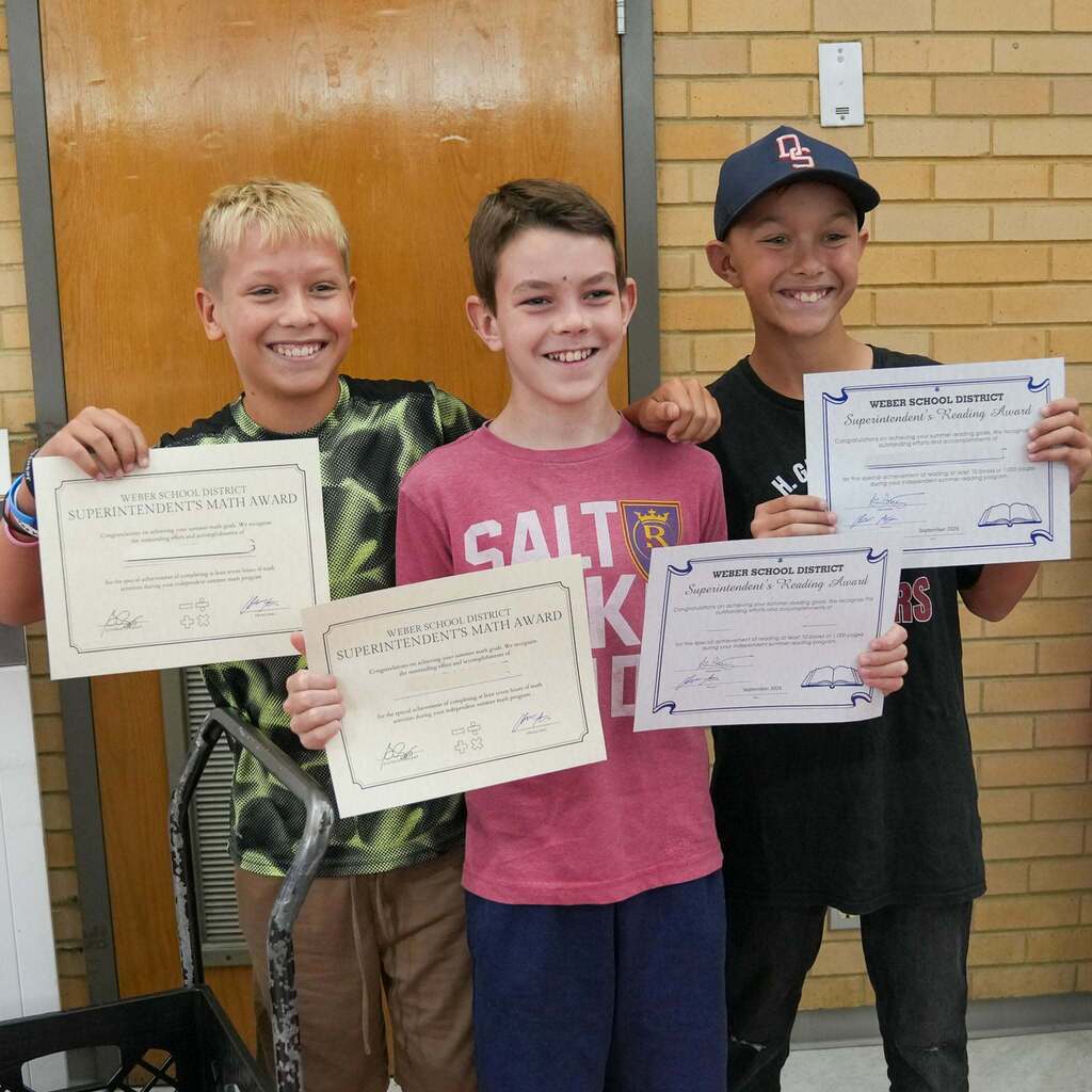 Image 8: Three smiling young male students standing together and proudly holding up their Weber School District Superintendent's Math Award and Reading Award certificates.
