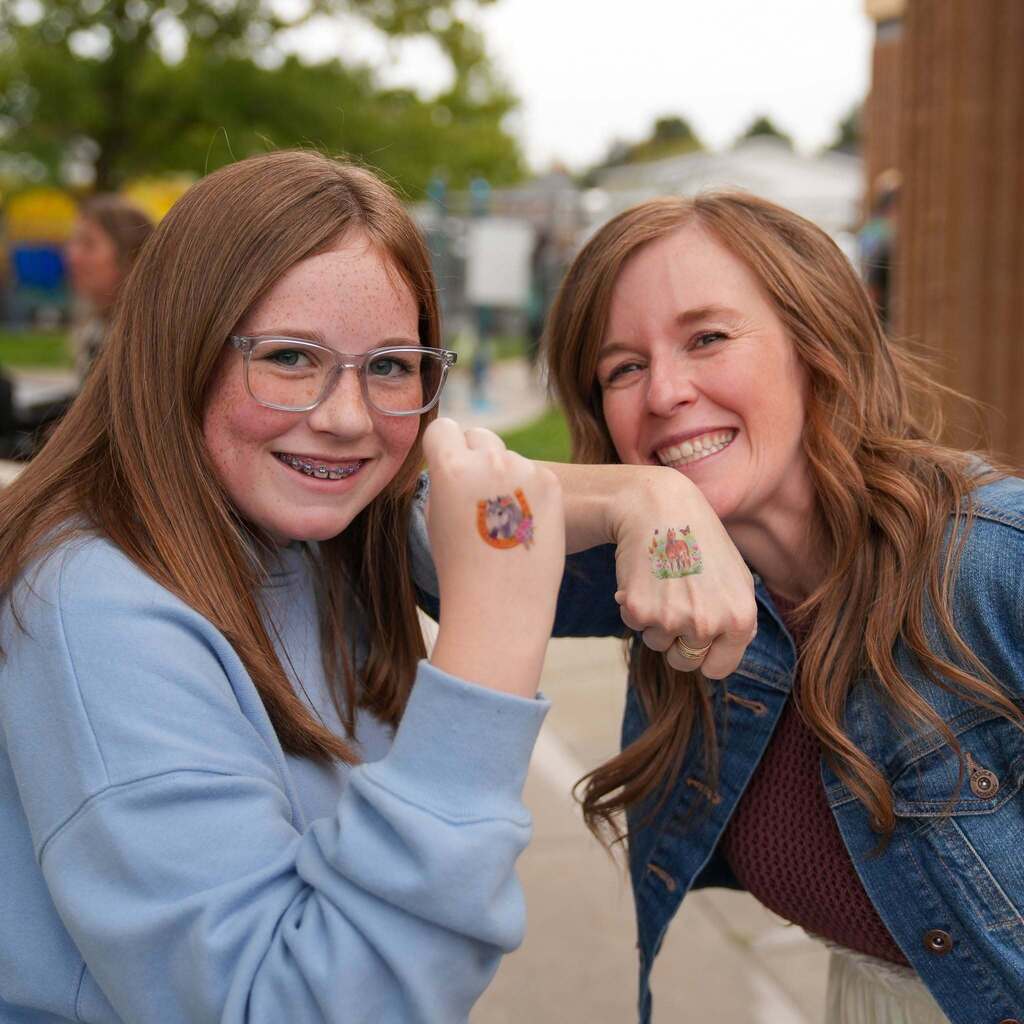 Image 2: A student with glasses and temporary hand tattoos smiling side-by-side with a school staff member wearing a denim jacket.