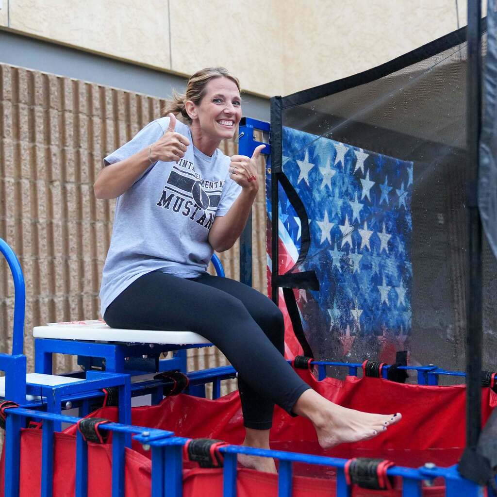 Image 4: A smiling staff member wearing a school shirt sitting over a dunk tank and giving a double thumbs-up.