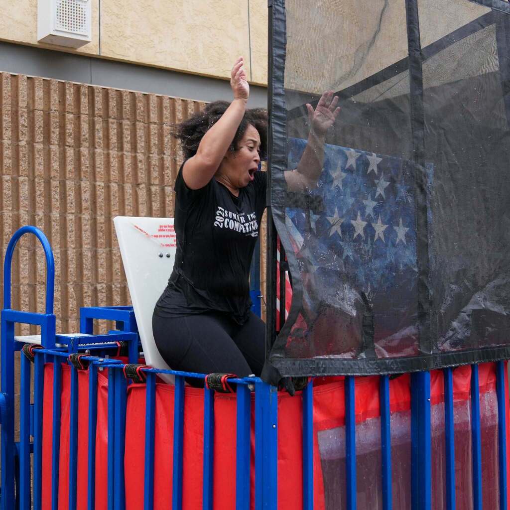 Image 6: A staff member reacting with excitement as she drops into a dunk tank full of water during a school event.