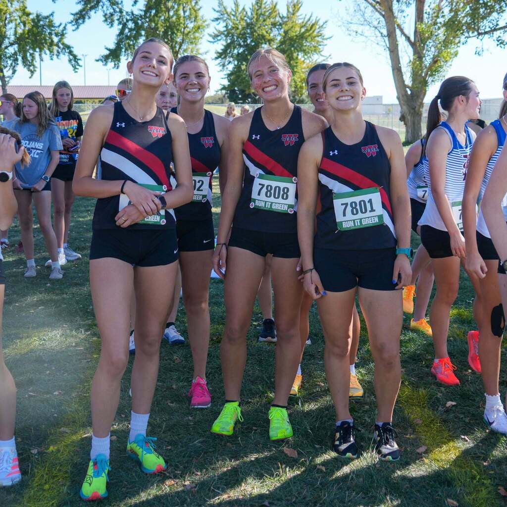 Image 1: Four student-athletes from the Weber High cross-country team smiling and posing together on the grass in their black, red, and white uniforms before a meet.