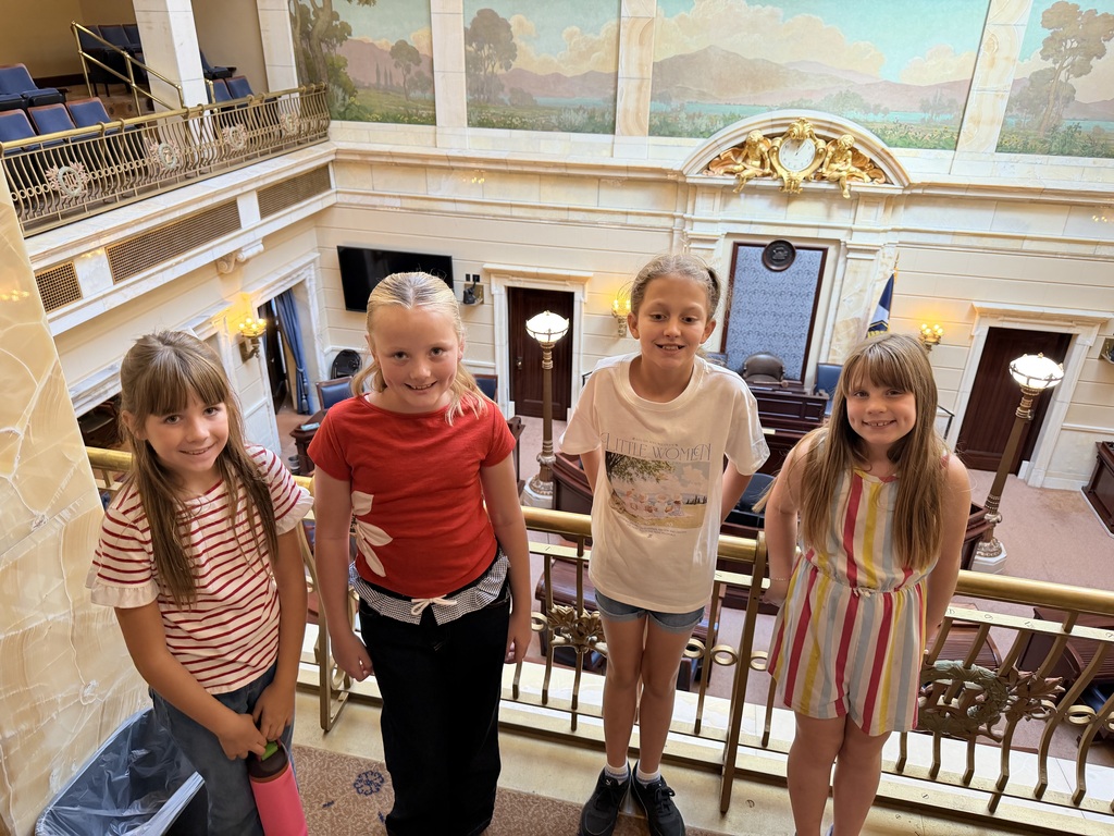 Four young girls posing smilingly along a golden balcony railing inside the Capitol Building.