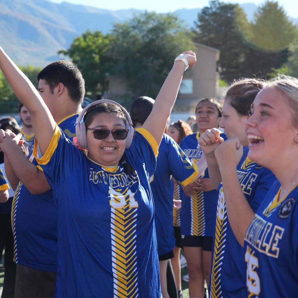 Image 5: A joyful Bonneville High athlete wearing headphones celebrating on the field with arms raised in the air alongside cheering teammates.