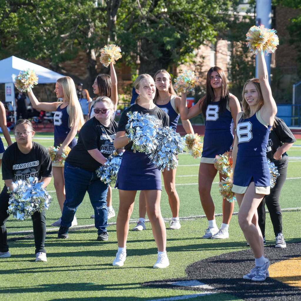 Image 3: Cheerleaders and Starbound Unified cheer team members holding pom-poms and performing a routine together on the field.