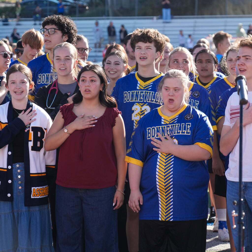 Image 4: Students and Unified Sports athletes standing in a row on the sideline field with their hands over their hearts during the national anthem.