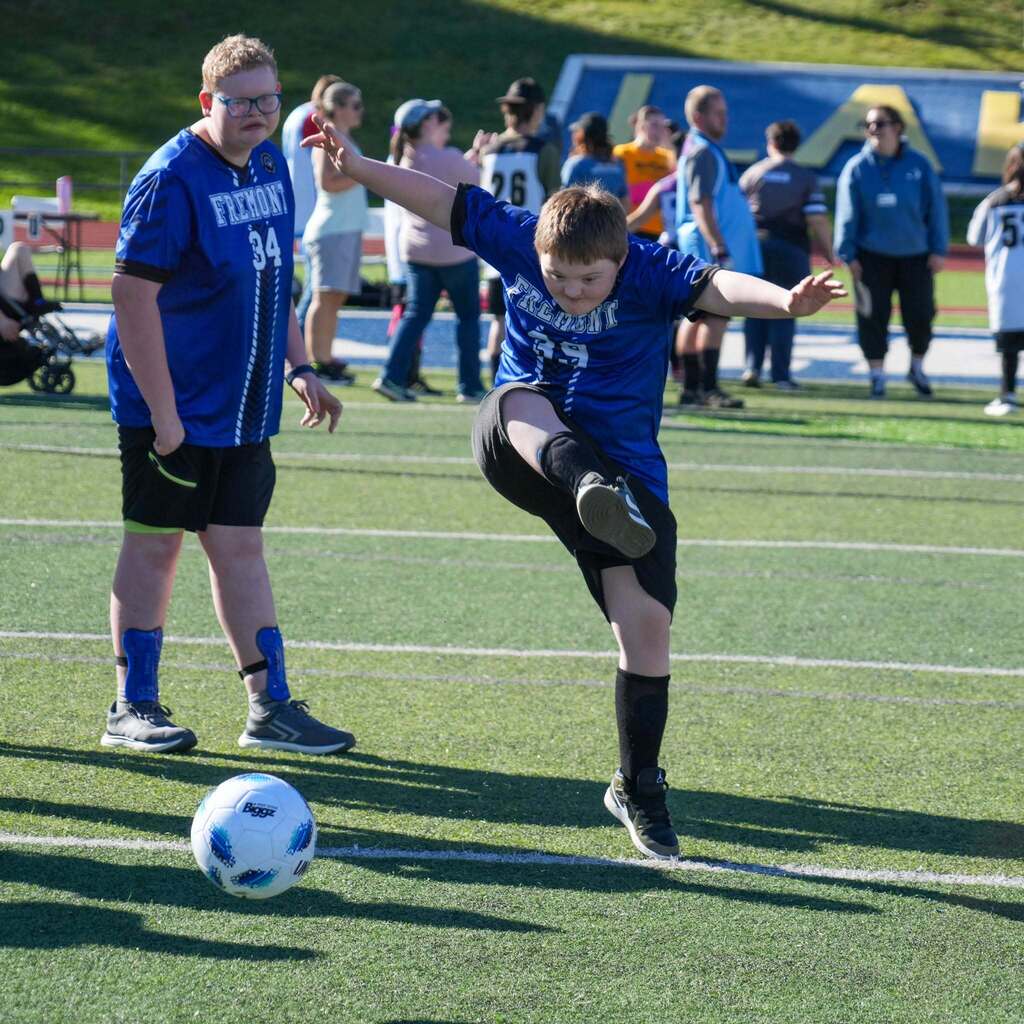 Image 7: A Fremont High Unified soccer player winding up to kick a soccer ball across the turf field while a teammate watches nearby.