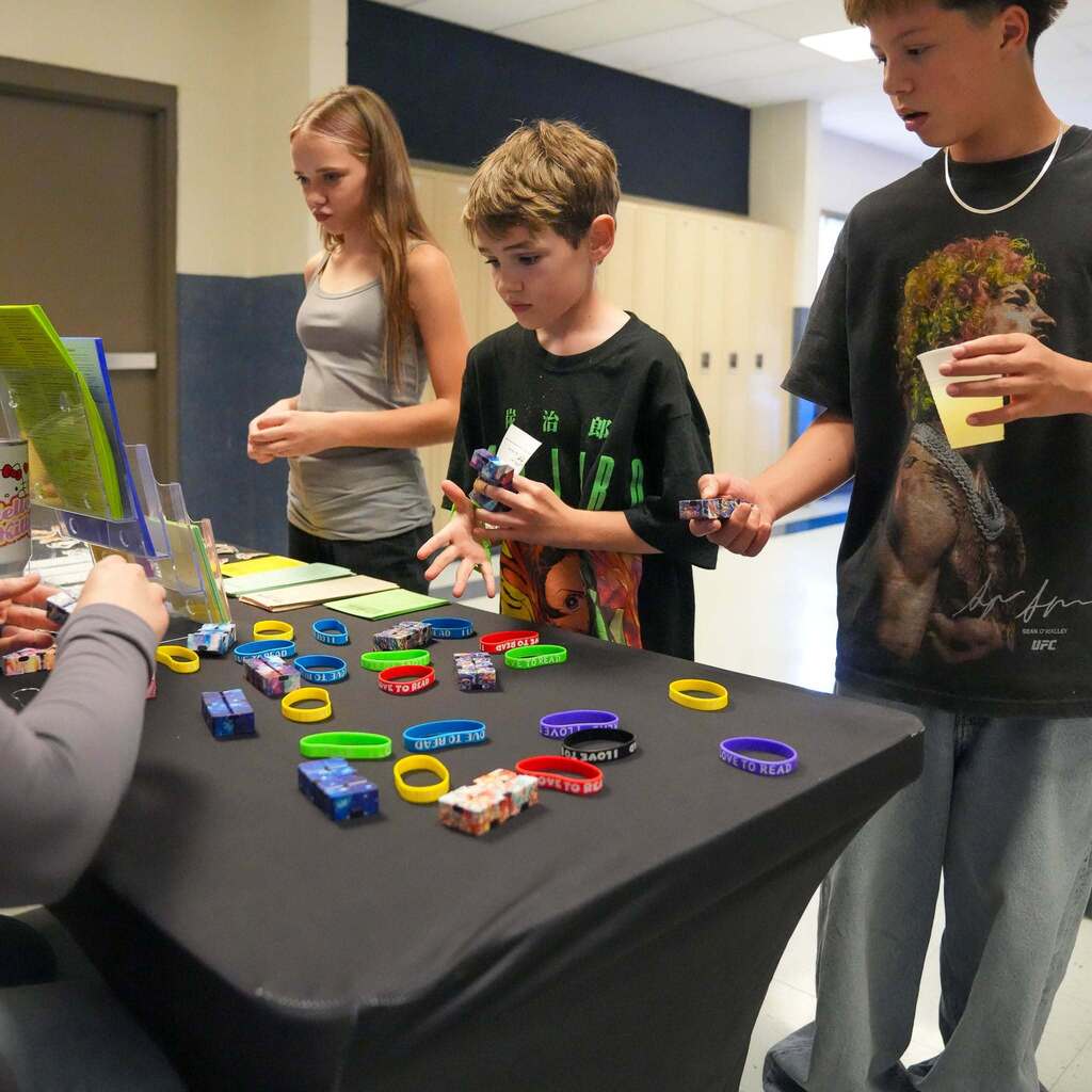 Image 9: Students examining reading prizes and silicone wristbands laid out on a table during the community reading event.