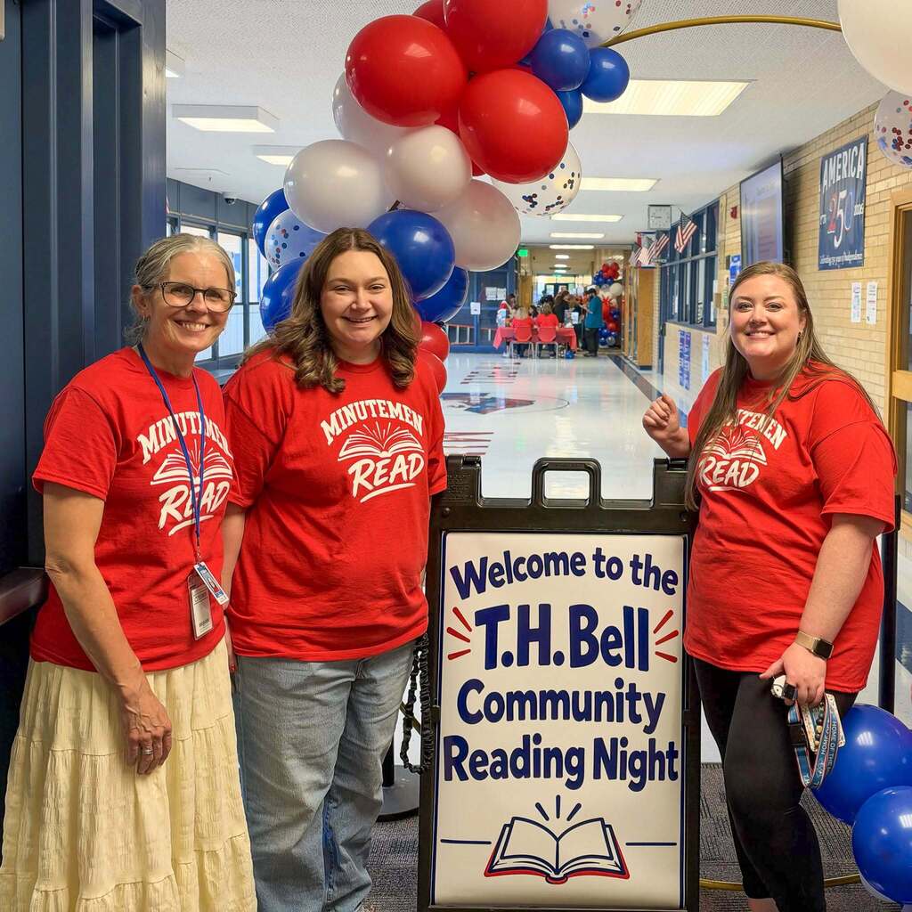 Image 1: Three smiling school staff members wearing matching red "Minutemen Read" t-shirts posing next to a welcome sign and balloon arch for T.H. Bell Community Reading Night.
