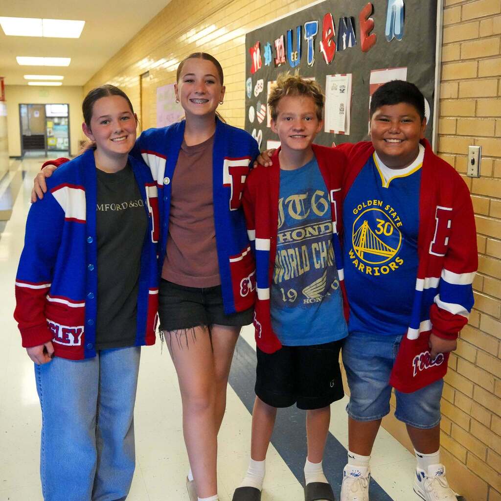 Image 3: Four smiling students wearing matching red, white, and blue letterman-style cardigans standing together in a school hallway.