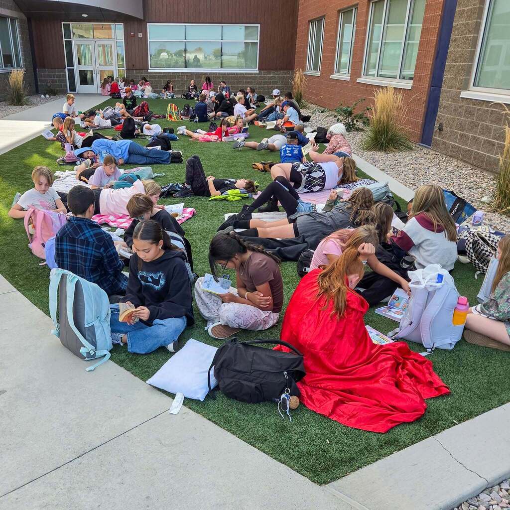 Image 2: A large group of students relaxing on blankets across a grassy outdoor courtyard area while reading books during a school reading event.