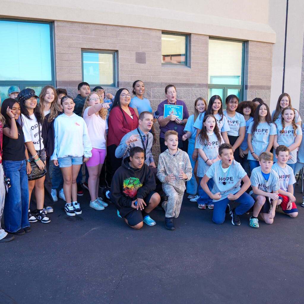 Image 3: A large group of elementary students, teachers, and Hope Squad members cheering and posing outside the school building with FOX 13 News.