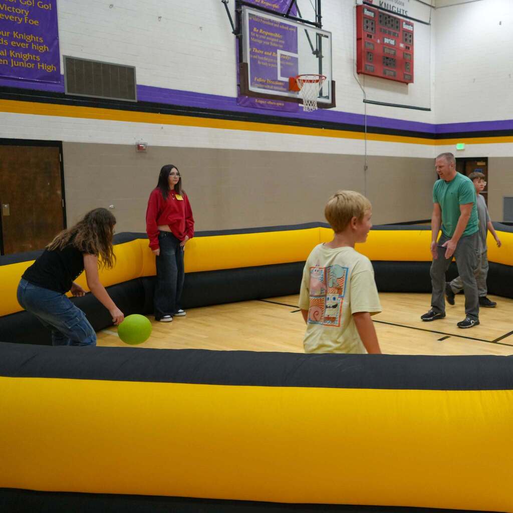 Image 6: Students and staff playing a friendly game of 9-square-in-the-air inside a gymnasium set up with a temporary inflatable arena.