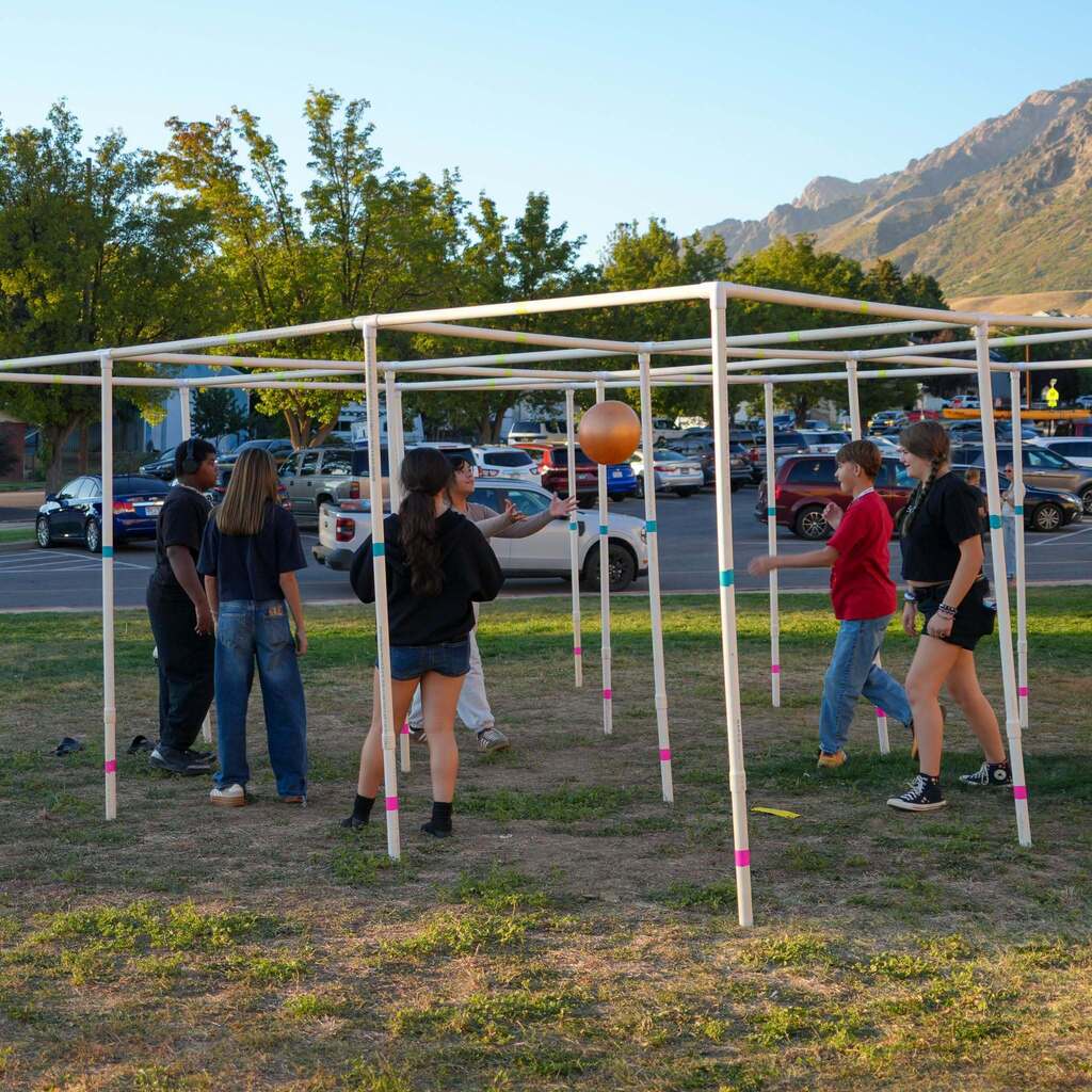 Image 10: A group of middle school students playing a game of 9-Square outdoors using a PVC pipe grid structure with mountains in the background.