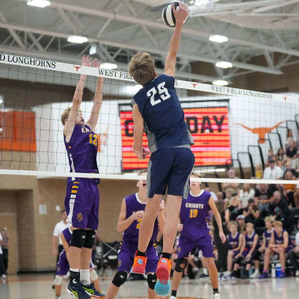 Image 10: An Orion Junior High volleyball player reaching high with one hand to strike the ball past a defender's block.