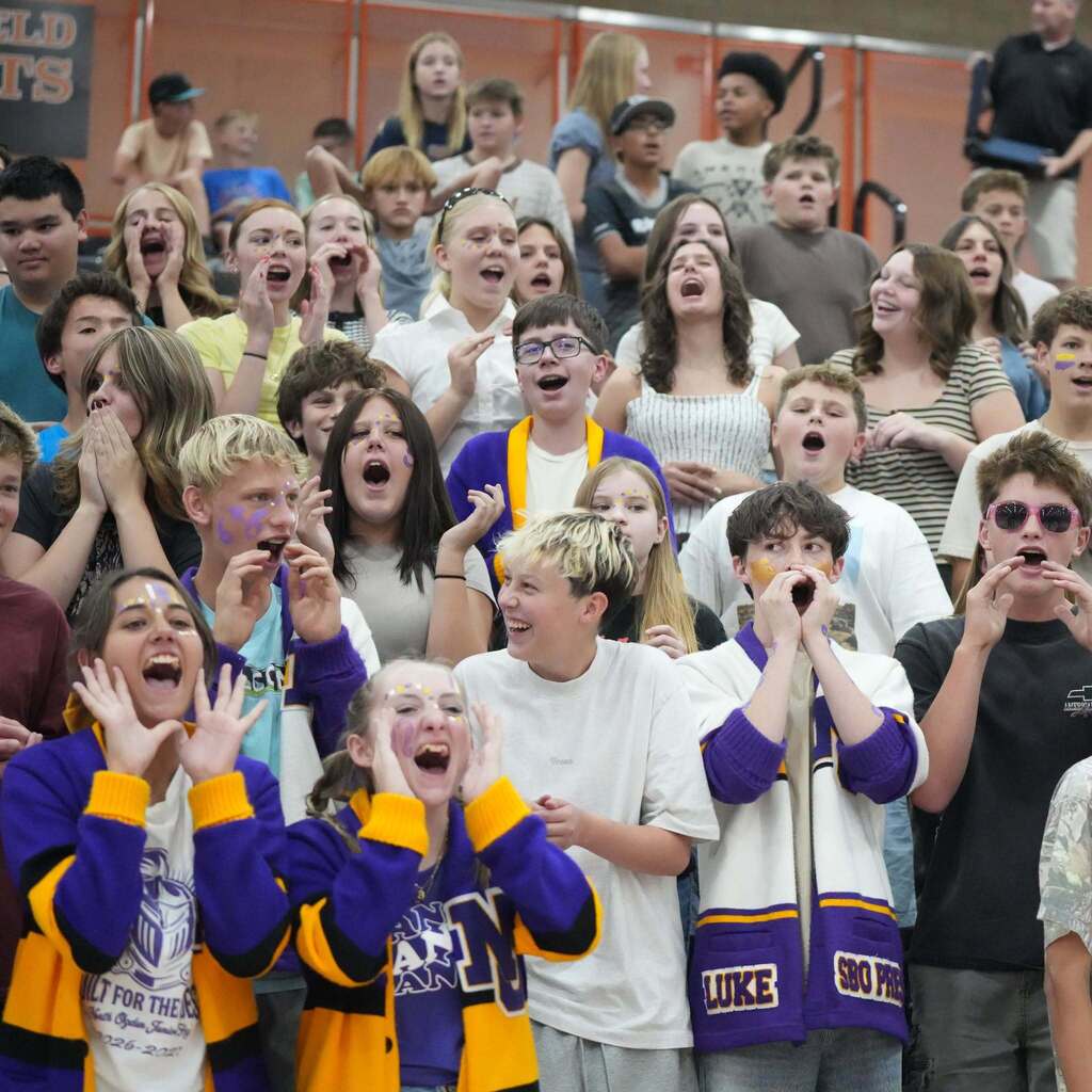 Image 6: A packed student section in the bleachers wearing school colors and wildly cheering during the championship match.
